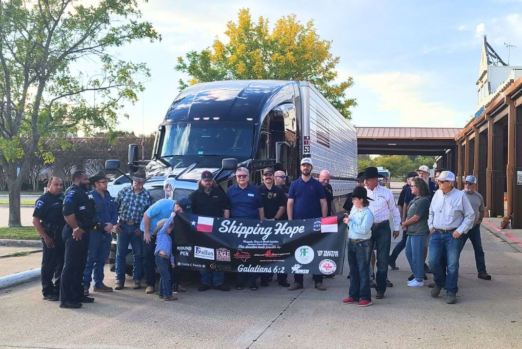 Image of a group of people standing in front of a Stevens Transport truck with a banner that says "shipping for hope"